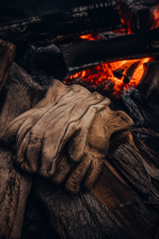 Leather fire gloves resting on firewood beside embers